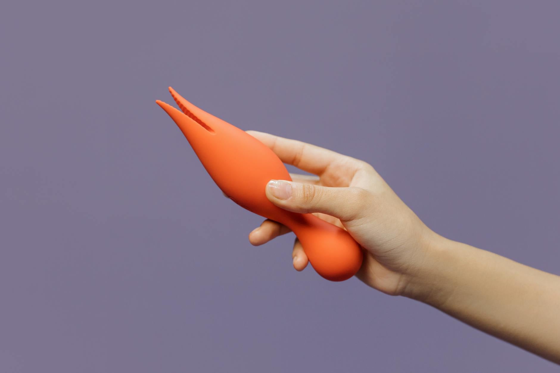 A hand holding a lemon clitoral vibrator against a minimalistic purple backdrop, showcasing modern sensuality